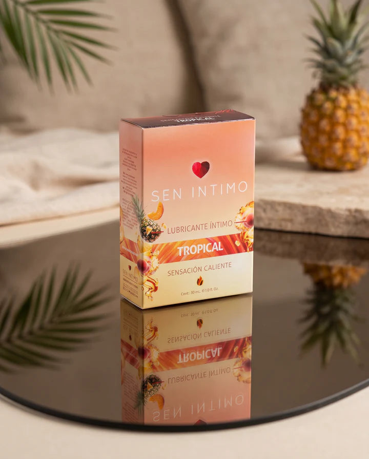 Caja del Lubricante Íntimo Tropical Caliente Sen Íntimo 30 ml sobre superficie reflectante con piña al fondo.