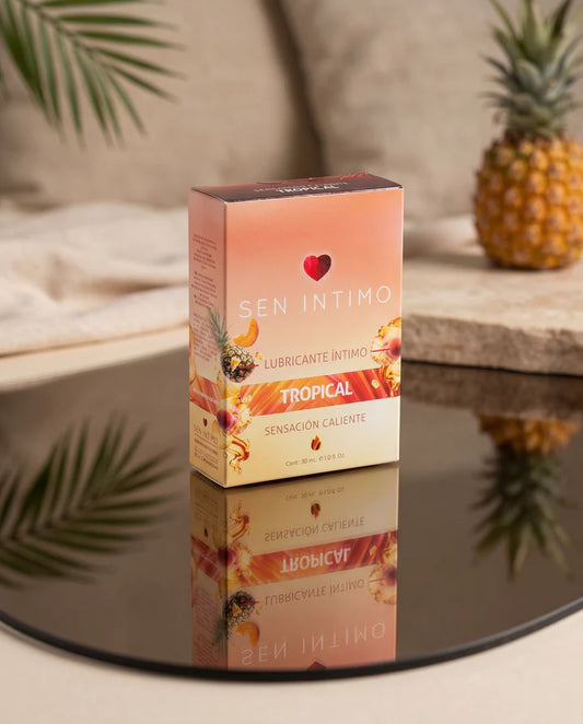 Caja del Lubricante Íntimo Tropical Caliente Sen Íntimo 30 ml sobre superficie reflectante con piña al fondo.